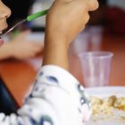 Criança se alimenta com um prato de comida a frente
