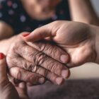 Mão de mulher segura a mão de uma pessoa idosa