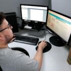Jovem de óculos segura mouse e olha para tela de computador