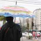 Homem anda com guarda chuva aberto em rua