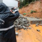 Agente da Defesa Civil com roupa para proteger da chuva fotografa área que sofreu deslizamento de terra