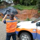 Agente da Defesa Civil, com colete laranja, fotografa área atingida por deslizamento de terra