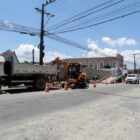 Caminhão e trator em rua em obras sinalizada por cones com carros transitando