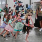 Crianças fantasiadas dançam observados por adultos