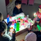 Crianças da educação infantil fazem atividade com garrafas pet em mesa iluminada
