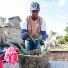 Agente de saúde com colete e luvas utiliza pinga líquido em vaso de flores em túmulo de cemitério