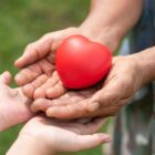 Mão de adulto segura um coração de borracha vermelho e estende para a mão de uma criança