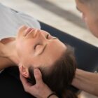 Mulher deitada de olhos fechados recebe massagem na cabeça por um profissional