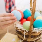 Mão de uma pessoa segura um ovo colorido de uma cesta cheia de ovos