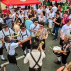 Pessoas com trajes típicos alemães tocam instrumentos musicais em uma rua