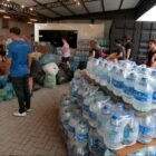 Área com doações, fardos de água, sacos com roupas e pessoas circulando