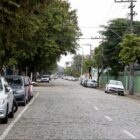 Imagem de uma rua de paralelepípedo, com carros estacionados